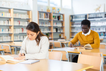 Young hispanic woman looking for information in books in libraryの写真素材