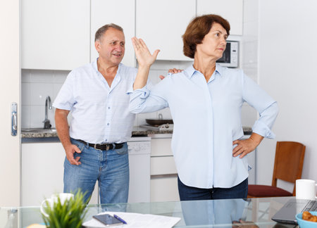 Sad mature female standing after qurrel with husband at home kitchenの写真素材