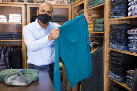 Man in mask choosing sweater in storeの写真素材