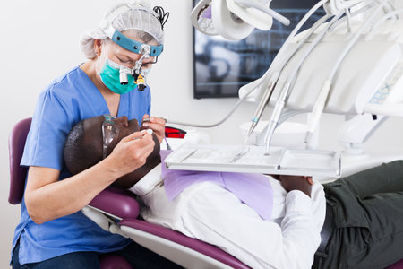 Dentist is treating male patient which is sitting in dental chairの写真素材