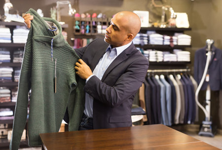 Confident man choosing sweater in clothing storeの写真素材