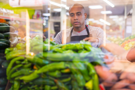 Spanish employee in vegetable store with green peppers