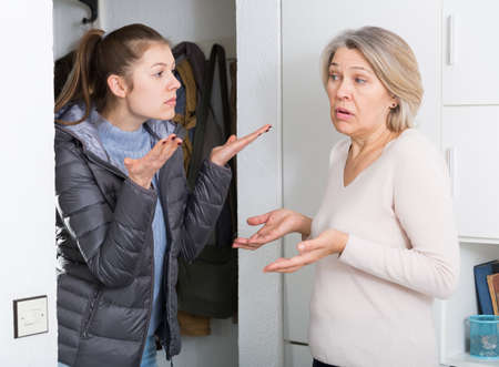 Mature mother and adult daughter quarrelling in entrance hallの写真素材