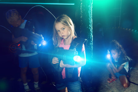 Portrait of teenager girl with laser gun having fun on dark lasertag arena
