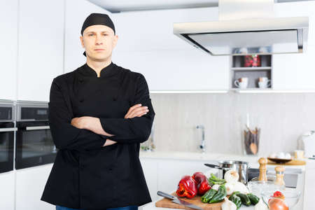 Smiling male kitchener in uniform is standing in the kitchenの写真素材