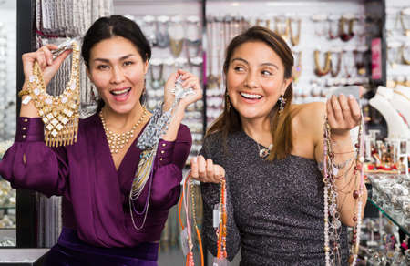 Two cheerful female customers showing necklaces in jewelry salonの写真素材