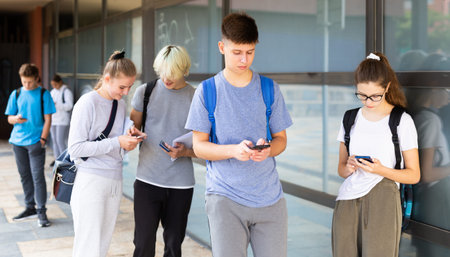 Students look at the screens of their smartphones on city streetの写真素材