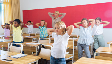 Preteen schoolchildren with teacher performing physical exercises in classroomの写真素材