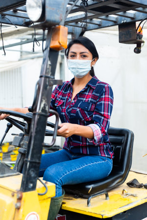 Female worker in protective mask of materials working on forklift truck