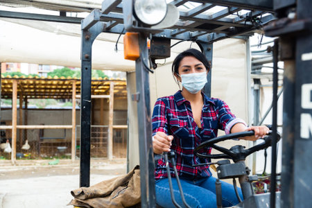 Masked hispanic woman sits behind the wheel of a tractor autocar during a pandemic.の写真素材