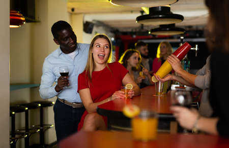 Couple of cheerful smiling male and female on party in the club with cocktailsの写真素材