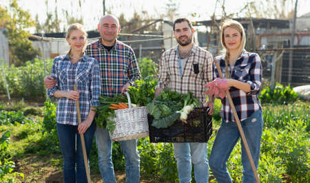 Family of four professional gardeners holding harvest of vegetables and greensの写真素材