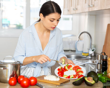 Housewife prepares tomato and avocado salad in the kitchen