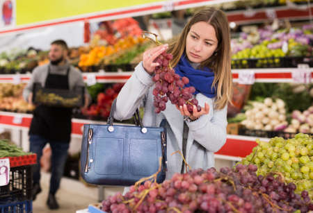 Female shopper picks grape at grocery storeの写真素材