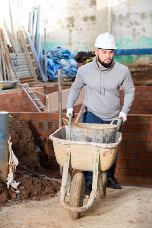 Guy in construction helmet carrying wheelbarrowの写真素材