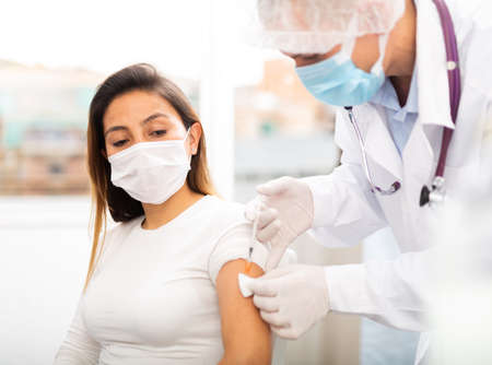 doctor in protective face mask vaccinates womanの写真素材