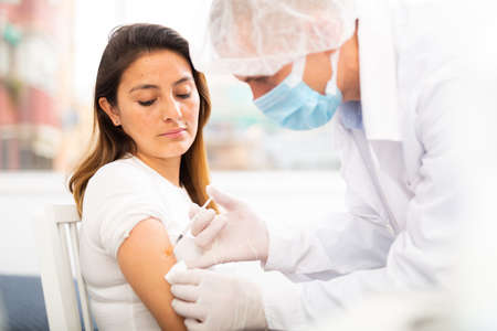 doctor in protective face mask vaccinates womanの写真素材