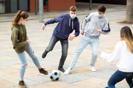 teenagers in protective face masks are playing footballの写真素材