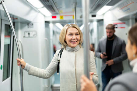 Mature woman talking with fellow traveler in subway carの写真素材