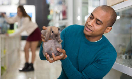 Joyful man tenderly holding a rabbit in his arms in pet storeの写真素材