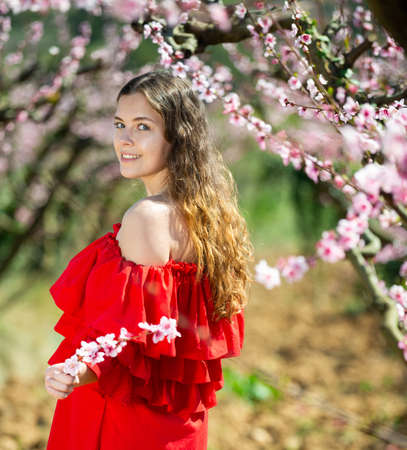 Woman in red dress standing near blooming peach treeの写真素材