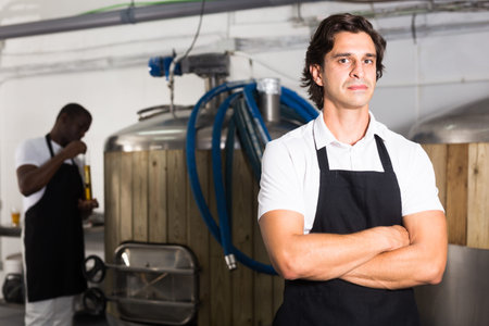 Young man brewer in uniform is standing in brew-houseの写真素材