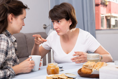 Emotional women having conflict at table with coffee in home