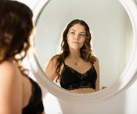 Girl in black lace bra looking at mirror in bedroom