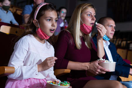 caucasian woman and girl in mask sitting at premiere in cinemaの写真素材