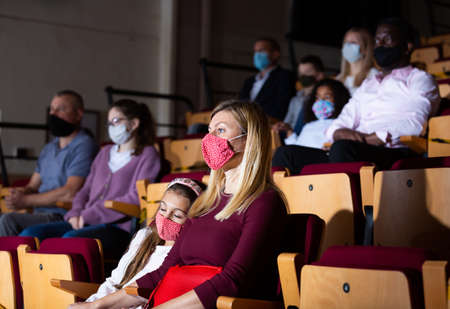 Woman with sleeping girl in protective mask watching theater performanceの写真素材