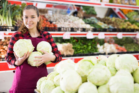 Young positive female seller displaying assortment of cabbagesの写真素材