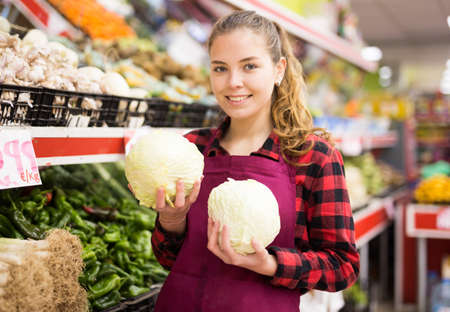 Portrait of a smiling girl of the seller holding a cabbage in her handsの写真素材