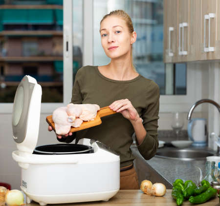 Smiling woman cooking with electric multicooker at home kitchenの写真素材