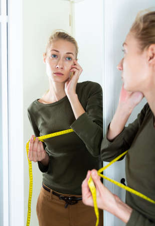 Smiling girl measuring bust with tape measure at homeの写真素材