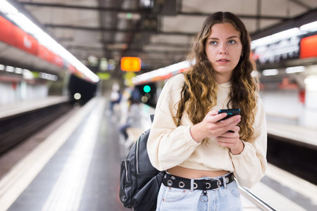 Thoughtful girl, walking along the platform of a subway station, holds a mobile phone