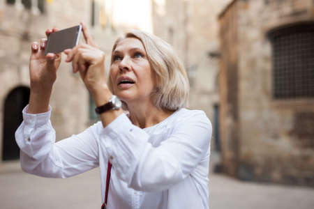 Mature woman is taking photos on her camera while journey through the cityの写真素材