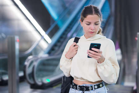 Young positive lady with smartphone standing on the escalatorの写真素材