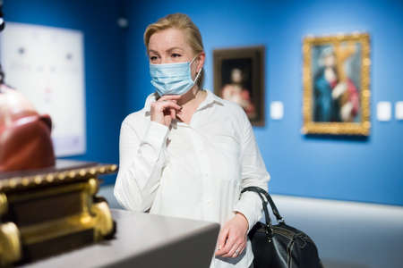 Adult woman in protective mask looking at exposition of artworksの写真素材