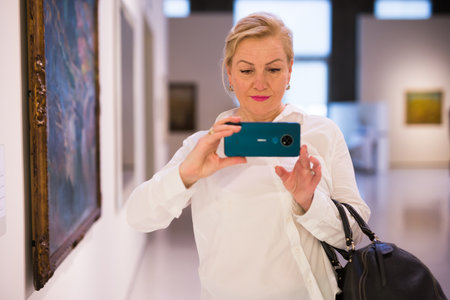 Female visitor taking picture in art galleryの写真素材