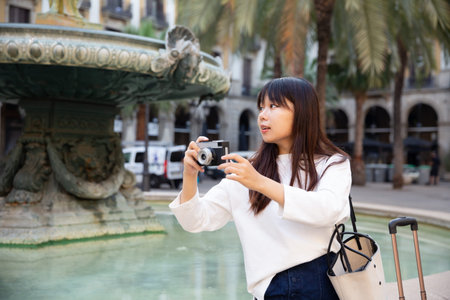 Smiling young girl holding camera in hands and photographing in city
