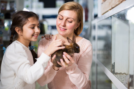 Mother with her daughter holding rabbit together at pet storeの写真素材