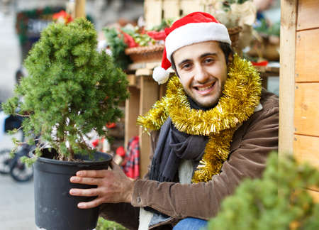 Portrait of joyful man choosing small Christmas tree at fairの写真素材