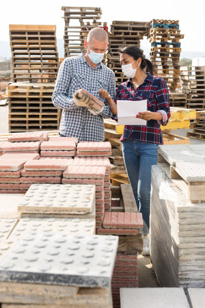 Man and woman in protective mask keep track of the number of paving slabs at the site of hardware...