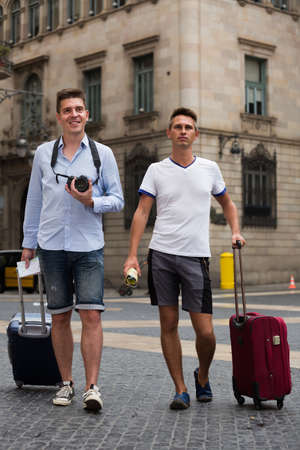 Male couples with travel bags walking the cityの写真素材