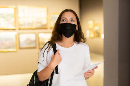 Young girl in a protective mask visits an exhibition of paintings in a museumの写真素材