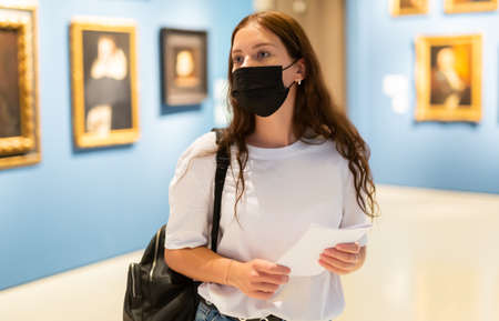 Young girl in a protective mask visits an exhibition of paintings in a museumの写真素材