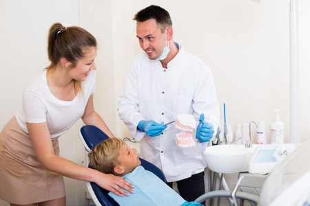 Stomatologist in uniform is telling to young boy and mother about healthcare