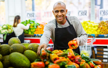 Supermarket employee lays out bell peppers on shelvesの写真素材