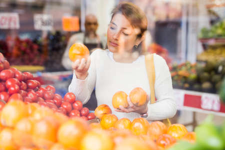 Portrait of latin american woman choosing ripe oranges in supermarketの写真素材