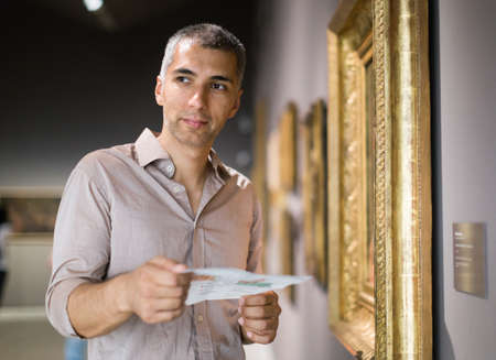 Adult man is visiting museum with information brochure and looking at the picturesの写真素材